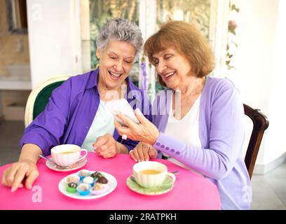 Zwei glückliche ältere Frauen, die im Café ein modernes Smartphone verwenden Stockfoto
