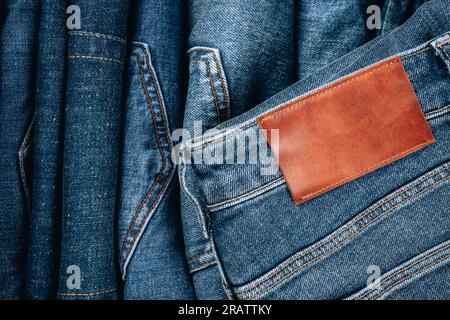 Unbeschriftetes braunes Lederetikett, das auf eine blaue Jeans genäht ist. Marineblauer Jeans-Anhänger. Draufsicht Stockfoto