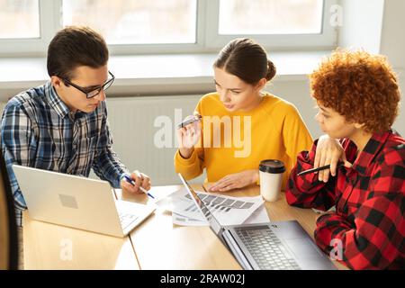 Fokussierte weibliche Teamleiterin bespricht Finanzstatistik, um ein Geschäftstreffen mit Partnerkunden im Büro zu organisieren. Junge Geschäftsfrau, Chefin. Vielseitiges professionelles Team Stockfoto