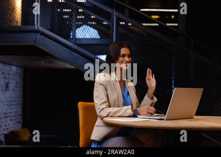 Glückliche Geschäftsfrau aus dem Nahen Osten, die ihren Laptop benutzt und im Büro winkt. Ungezwungenes Büro, Business, Lifestyle, Kommunikation und Arbeit, unverändert. Stockfoto