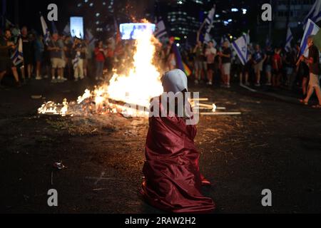 Tel Aviv, Israel. 05. Juli 2023. Eine Frau, die als Figur aus der TV-Serie "Tale" der Magd verkleidet ist, sitzt während Demonstranten den Highway blockieren, während sie gegen die Pläne der Regierung von Premierminister Benjamin Netanjahu protestieren, das Justizsystem zu reformieren. Kredit: Ilia Yefimovich/dpa/Alamy Live News Stockfoto