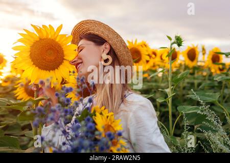 Nahaufnahme eines Porträts einer jungen Frau, die in einem blühenden Sonnenblumenfeld bei Sonnenuntergang nach Blumen duftet. Sommer in der Ukraine. Leerzeichen Stockfoto