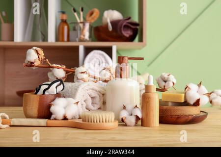 Set aus Kosmetikprodukten, Badzubehör und Baumwollzweig auf Holztisch in der Nähe von Farbwänden Stockfoto