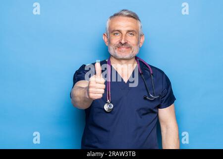 Mittelalter grauhaariger Arzt, der Daumen hoch über isoliertem blauem Hintergrund macht Stockfoto