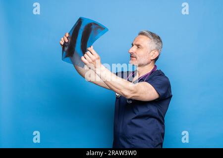 Lächelnder Arzt hält Röntgenbild auf blauem Hintergrund Stockfoto