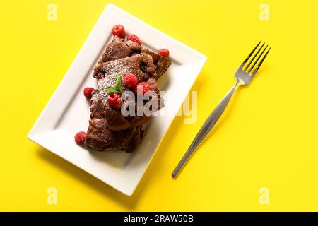Teller mit Himbeer-Schokoladen-Brownie auf gelbem Hintergrund Stockfoto