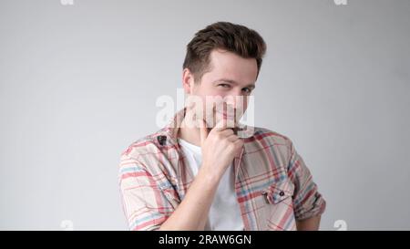 Ein junger Mann ist tief in Gedanken und kratzt sich am Kinn, während er versucht, etwas auszuwählen Stockfoto