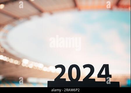 Die Silhouette des „2024“-Schriftzugs inspiriert zum Beginn des Sportjahres und führt zu den Sommerspielen in Paris. Modernes Stadion im Hintergrund. Stockfoto