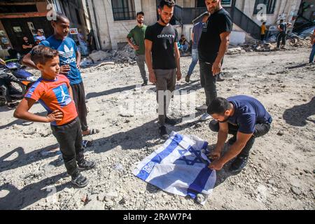 Dschenin, Palästina. 05. Juli 2023. Palästinenser verbrennen eine israelische Flagge inmitten der Ruinen im Zentrum des Flüchtlingslagers Dschenin in der Nähe der Stadt Dschenin im nördlichen Westjordanland. Der Rückzug der Truppen aus dem Lager beendete eine intensive zweitägige Operation, bei der mindestens 13 Palästinenser ums Leben kamen, Tausende von Menschen aus ihren Häusern vertrieben wurden und ein großer Teil der Schäden hinterließ. Ein israelischer Soldat wurde ebenfalls getötet. (Foto von Nasser Ishtayeh/SOPA Images/Sipa USA) Guthaben: SIPA USA/Alamy Live News Stockfoto