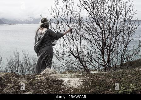 Mittelalterliche Frau, die über einen Fjord schaut. Künstlerische Farben rufen eine magische, fantastische Welt hervor, in die wir alle gerne für einen Tag entfliehen würden. Stockfoto