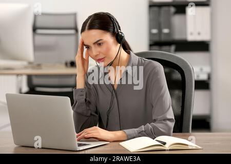 Gestresster Hotline-Mitarbeiter mit Headset, der im Büro auf einem Laptop arbeitet Stockfoto