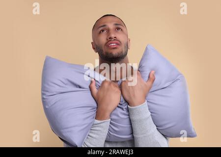 Ein unglücklicher Mann mit einem Kissen auf beigem Hintergrund. Schlaflosigkeit-Problem Stockfoto