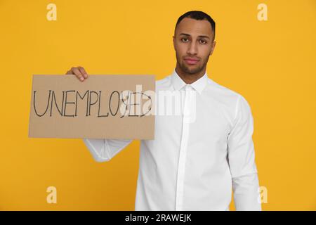 Junger Mann mit Schild mit dem Wort arbeitslos auf gelbem Hintergrund Stockfoto