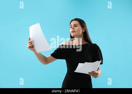 Emotionale Schauspielerin mit Drehbuch auf hellblauem Hintergrund. Filmindustrie Stockfoto
