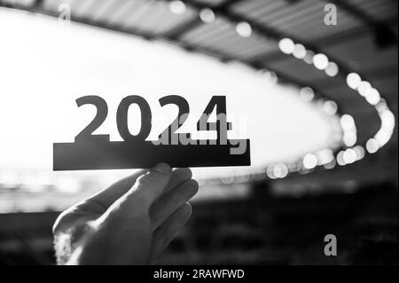 Silhouette von „2024“ in der Hand von Athleten. Das Zeichen signalisiert den Beginn des Sportjahres und führt zu den Sommerspielen in Paris. Modernes Sportstadion hinten Stockfoto