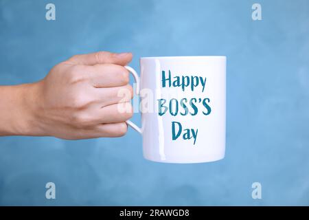 Eine Frau, die einen Becher mit dem Ausdruck Happy Boss's Day auf hellblauem Hintergrund hält, Nahaufnahme Stockfoto