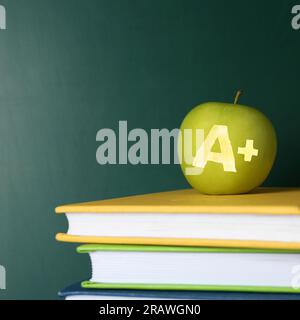 Apfel mit geschnitztem Buchstaben A und Plus als Schulklasse in Büchern nahe der grünen Tafel, Platz für Text Stockfoto