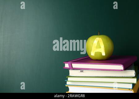 Apfel mit geschnitztem Buchstabe A als Schulklasse in Büchern nahe der grünen Tafel, Platz für Text Stockfoto