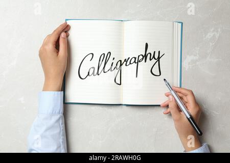 Frau schreibt das Wort Kalligraphie in Notizbuch am Marmortisch, Draufsicht Stockfoto