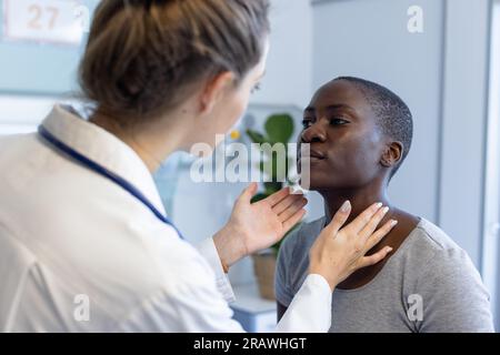 Vielfältige Ärztin und Patientin, die die Patientin untersucht, den Hals im Krankenhaus berührt. Krankenhaus-, Medizin- und Gesundheitsdienstleistungen, unverändert. Stockfoto