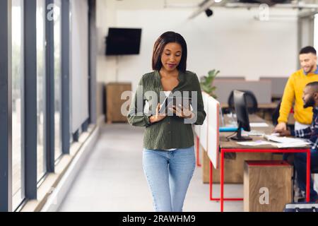 Glückliche Geschäftsfrau, die ein Tablet mit Kollegen im Büro verwendet. Ungezwungene Geschäfte, Kommunikation und Arbeit, unverändert. Stockfoto