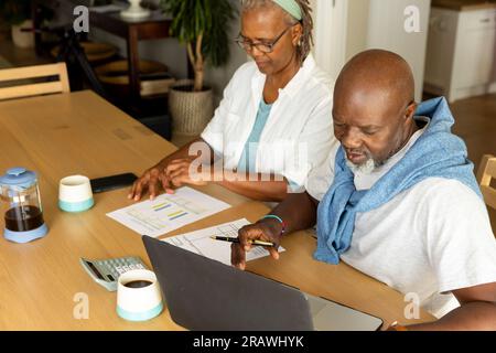 Glückliches Senior-afroamerikanisches Paar, das mit dem Laptop am Tisch saß und zu Hause Rechnungen bezahlte. Lebensstil älterer Menschen, Finanzen, Ruhestand und Familienleben, Stockfoto