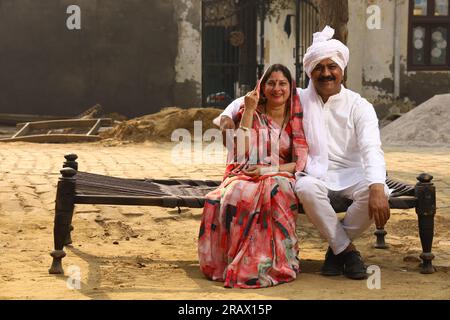 Ein alter Mann, der in der ländlichen Umgebung sitzt und Kurta-Pyjama trägt, was ein traditionelles Kleid für Männer in Nordindien ist, wenn er tagsüber mit seiner Frau unterwegs ist. Stockfoto