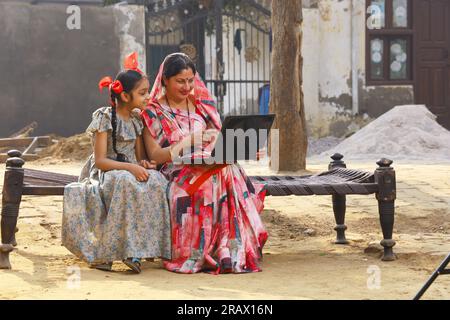 Frau, die im ländlichen Raum sitzt und Saree trägt, Sari, ein traditionelles Kleid für Frauen in Nordindien, mit einem Laptop in der Hand. Stockfoto