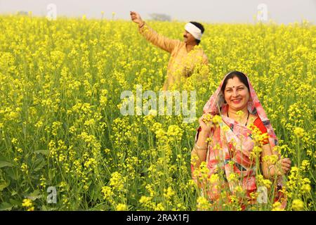 Glückliche indische Landfamilie, die auf einem Senffeld steht. Ich freue mich über die landwirtschaftlichen Verdienstvorteile. Stockfoto