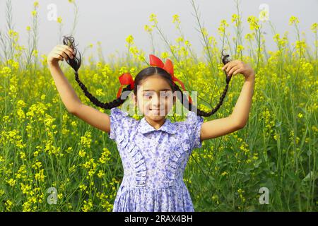 Glückliches, ländliches indisches Mädchen, das auf einem wunderschönen Senffeld steht, gefüllt mit wunderschönen gelben Blumen Stockfoto