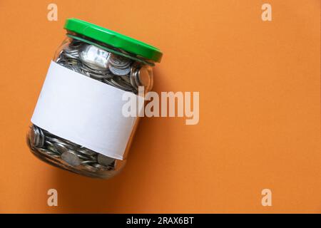 Glasbehälter mit ukrainischen Münzen auf braunem Papierhintergrund, Nahaufnahme Stockfoto