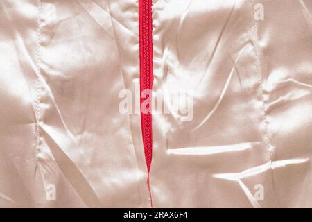Weißes, zerknittertes Seidenmaterial als Nahaufnahme des Hintergrunds mit rotem Reißverschluss in der Mitte Stockfoto