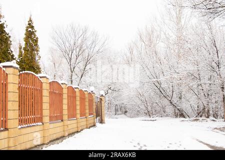 Ziegelzaun mit Toren vor dem Hintergrund eines Winterwaldes im Schnee in der Ukraine Stockfoto