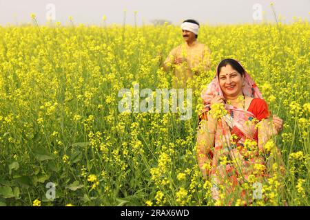 Die ländliche indische Familie, die auf dem Senffeld steht, und sowohl Mann als auch Frau freuen sich über die landwirtschaftlichen Vorteile des Feldes. Stockfoto