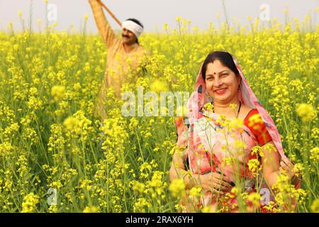 Die ländliche indische Familie, die auf dem Senffeld steht, und sowohl Mann als auch Frau freuen sich über die landwirtschaftlichen Vorteile des Feldes. Stockfoto