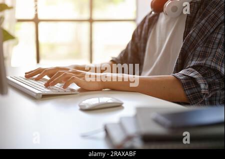 Nahaufnahme eines männlichen Programmierers oder Freiberuflers in einem Flanellhemd, der seinen Computer verwendet, auf der Tastatur tippt, an seinem Projekt an einem Computer in t arbeitet Stockfoto