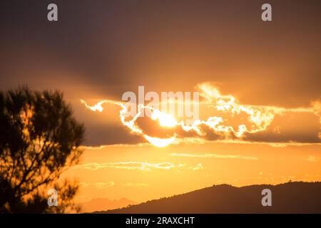 Sonne, halb hinter Wolken bei Sonnenuntergang in der Sierra de Mariola, Valencian Community Stockfoto