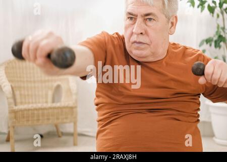 Alter Alter Mann in Sportbekleidung Training im Wohnzimmer, Gewichtheben Kurzhantel Training zu Hause, Freizeit gesunder Lebensstil. Ein älterer Mann ist ein Arbeiter Stockfoto