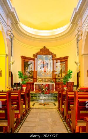 Guadalest, Alicante, Spanien - 14. Januar 2023: Ein Kircheninnere mit Bänken, die zum Altar führen. Die Bänke sind aus Holz. Stockfoto