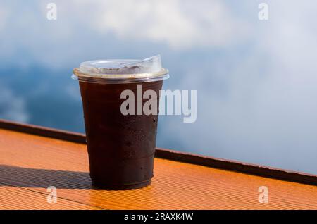 Ein Glas Eiskaffee mit Eiswürfel wird mit Himmel und Wolken auf den Tisch gestellt. Sommergetränk-Konzept. Stockfoto