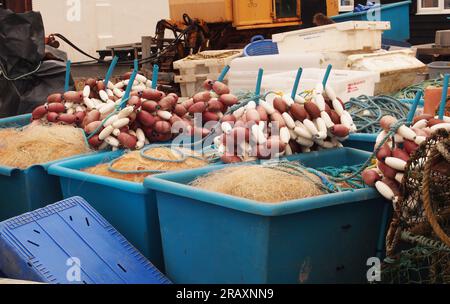 Kisten mit feinen Schleppnetzen und schwimmenden Schiffen am Kieselstrand in Adeburgh, Suffolk. UK und andere Gegenstände für die Seefischerei. Stockfoto