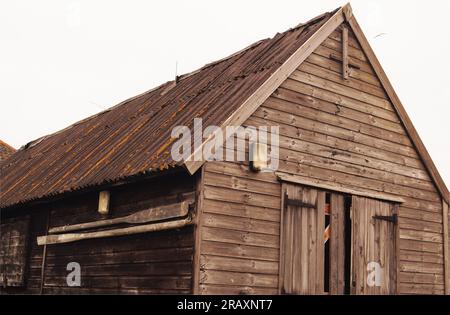 Ein Paar lange, alte, hölzerne Ruder für ein Ruderboot, an der Seite eines großen Holzschuppens mit einem Welleisendach in Aldeburgh, Sukkolk. UK Stockfoto