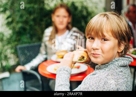 Die Familie isst draußen auf einer Terrasse zu Mittag, im Hintergrund wird gegessen, Kinder essen Humburger Stockfoto