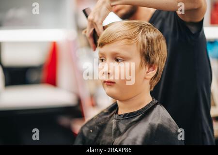 Ein kleiner Junge bekommt einen neuen Haarschnitt im Friseursalon Stockfoto