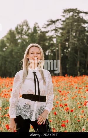 Außenporträt einer schönen Frau mit blondem Haar, trägt weiße Bluse, posiert im Mohnfeld Stockfoto