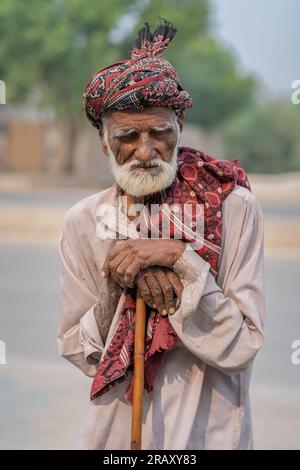 Halbkörperporträt eines alten Sindhi mit weißem Bart, traditionellem Ajrak-Turban und Schal und Bambus-Wanderstock Stockfoto