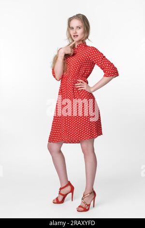 Blonde Frau in Sommerkleid mit roten Punkten, rote Schuhe in voller Länge und Posen auf weißem Hintergrund. Authentizitätsmodell 21 Jahre alt Stockfoto