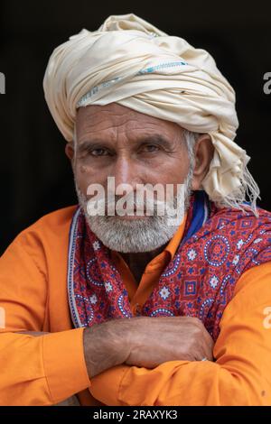 Attraktiver pakistanischer Mann mittleren Alters mit Bart und orangefarbenem Hemd in traditionellem weißem Turban und Ajrak-Schal auf schwarzem Hintergrund Stockfoto