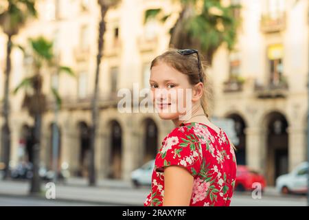 Junge Touristenfrau, die durch die Straßen von Barcelona spaziert, in rotem Kleid Stockfoto