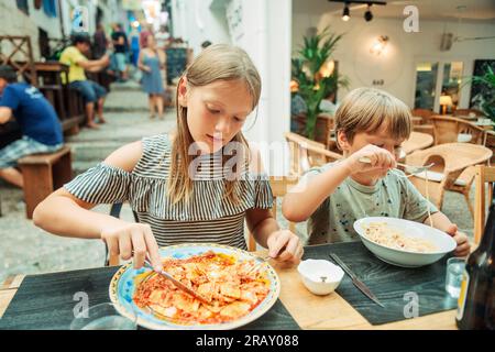 Zwei lustige Kinder essen im Restaurant zu Mittag und essen Ravioli und Pasta Stockfoto